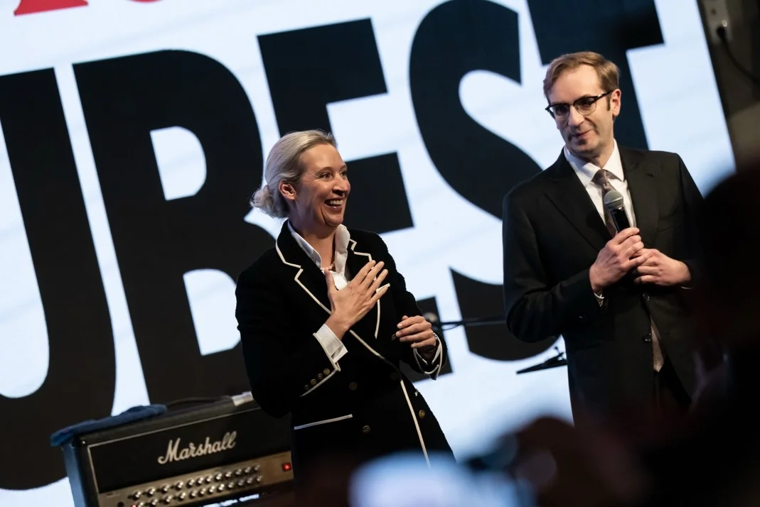 Photo by Alice Weidel on February 17, 2026. May be an image of one or more people, microphone and text.