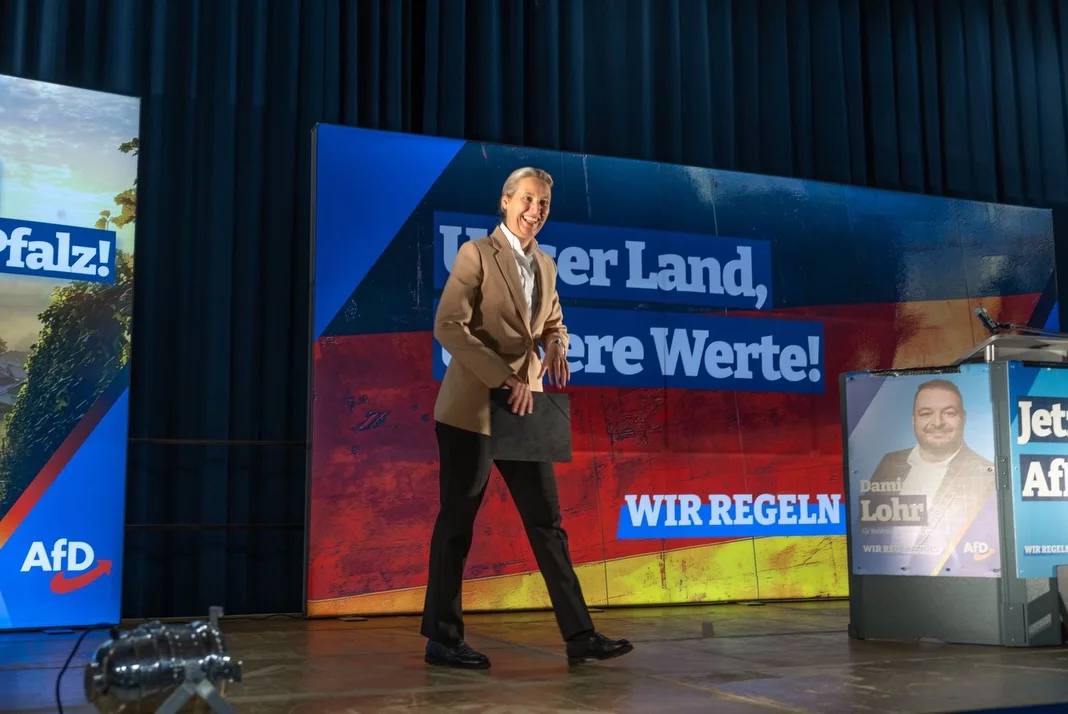 Photo by Alice Weidel on February 21, 2026. May be an image of microphone, newsroom and text that says 'falz! MerLand, er Land, ere Werte! AfD Jet Af WIR WIRREGELN Dami REGELN Lohr WIRRBGGATAS 5o o AfD. REGELI'.