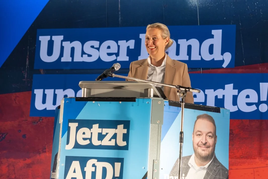 Photo by Alice Weidel on February 21, 2026. May be an image of microphone and text that says 'Unseri serlnd, nd, uni un" prte! Jetzt Afi'.