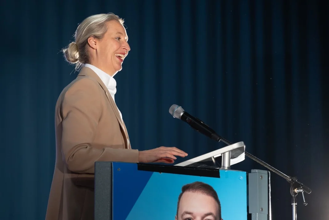 Photo by Alice Weidel on February 21, 2026. May be an image of one or more people, microphone and text.